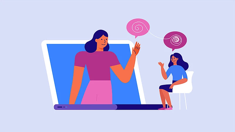 A woman sitting in a chair converses with a large woman emerging from a laptop screen.