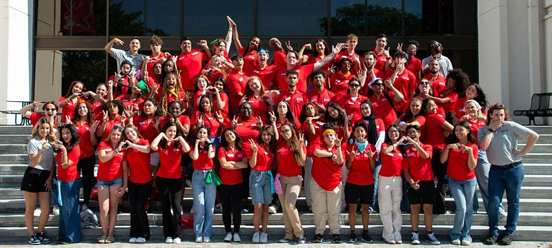 A large group of people wearing red shirts pose enthusiastically on steps in front of a building.