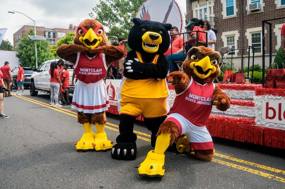 Three college mascots in costume pose together in a festive parade scene with Montclair State University branding visible.